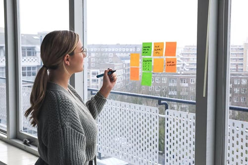 Vrouw schrijft ideeën voor het werven van nieuwe medewerkers op post-its die op raam plakken.